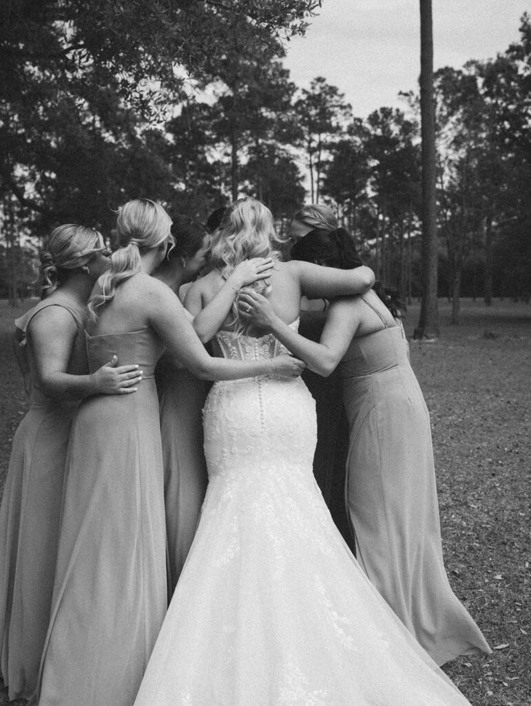 Bridesmaids hugging the bride during their first look for candid wedding photos.