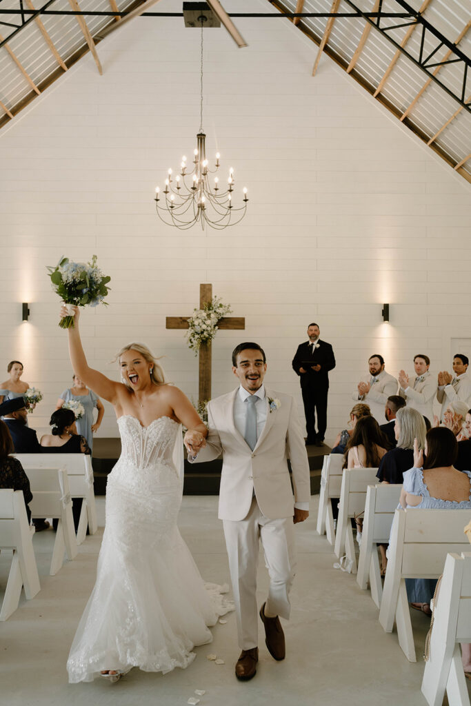 Bride and groom skipping and cheering as they walk down the aisle for candid wedding photos.
