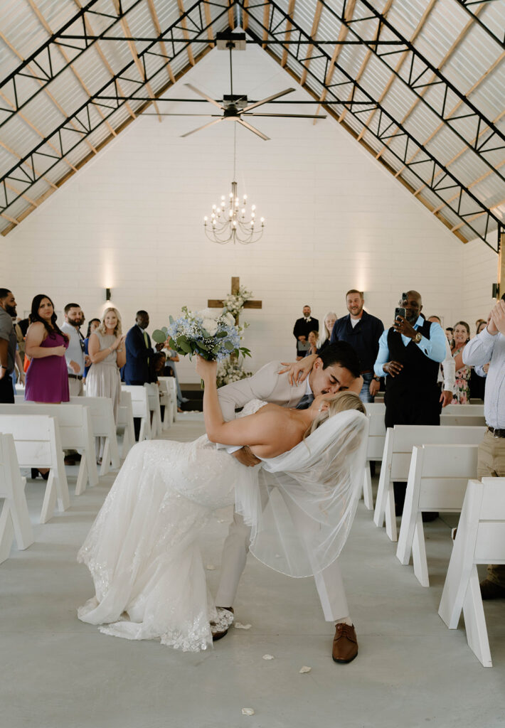Groom kissing his bride at the end of the aisle.