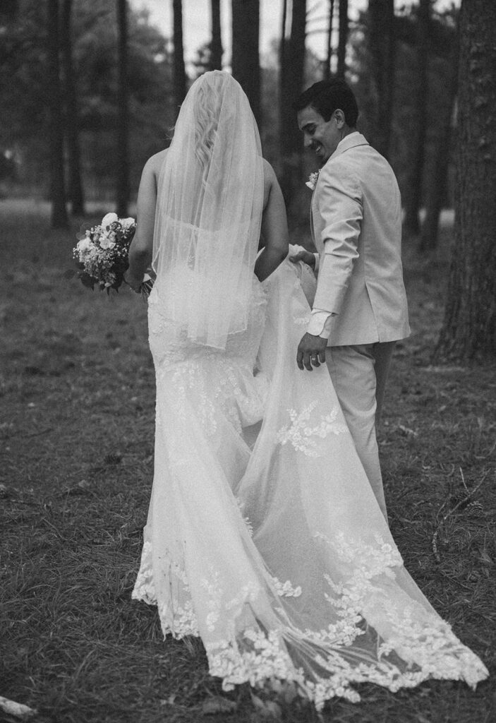 Groom holding the bride's train as they walk outside.