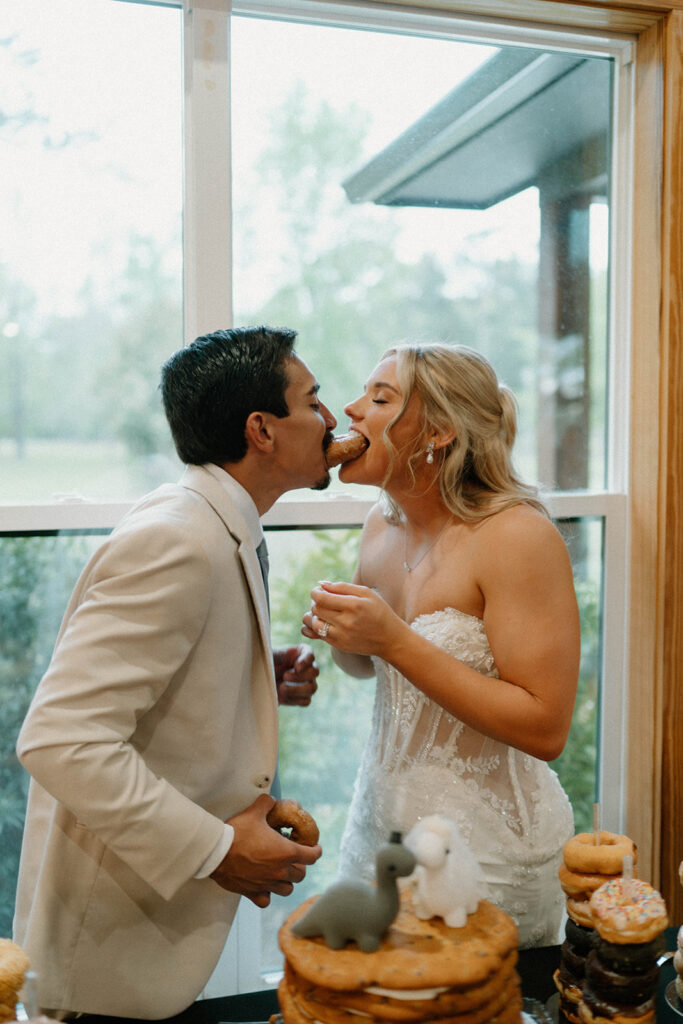 Candid wedding photos of bride and groom biting into a donut. 