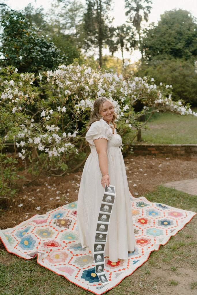Woman smiling while standing on a baby blanket for pregnancy announcement photos.