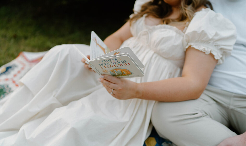 A couple laying on a blanket while reading a children's book.