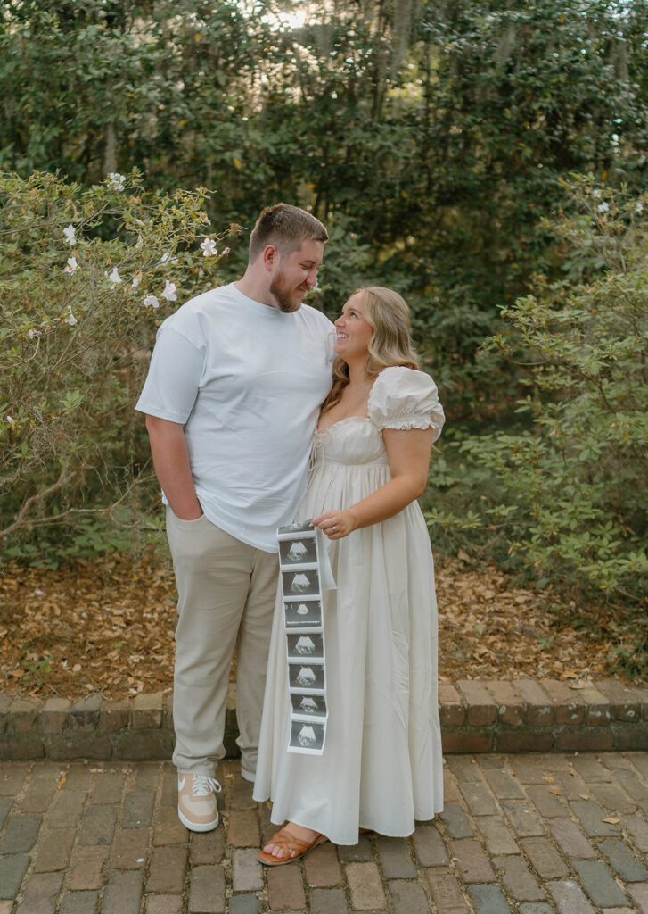 Couple holding an ultrasound photo strip and smiling at one another.