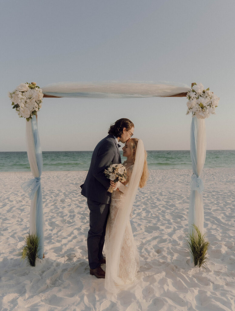 A groom kissing his bride's forehead during their beach elopement. 
