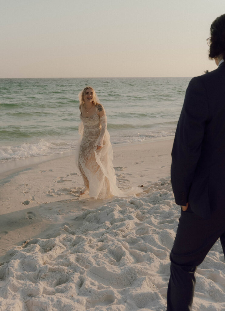 A bride walking towards the ocean, laughing.