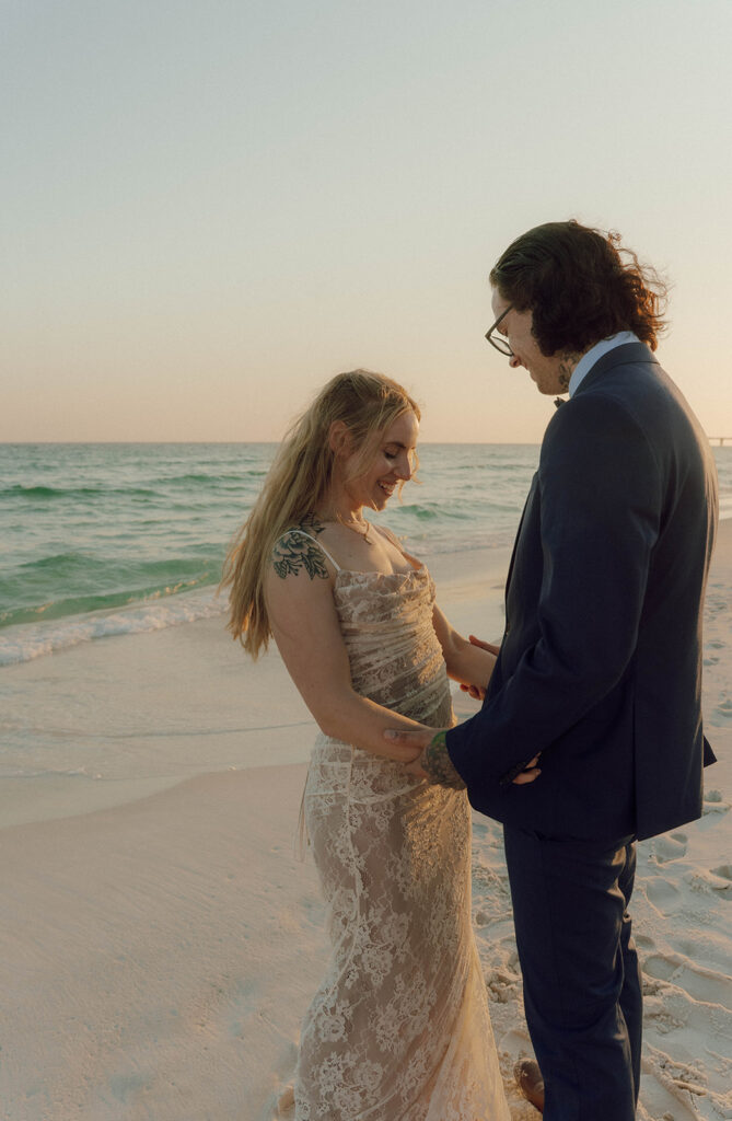 Bride and groom holding hands by the ocean.