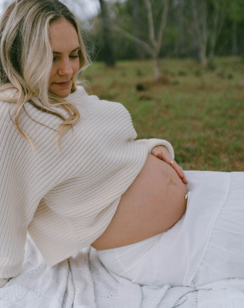 A woman sitting on a blanket with her hand on her belly.