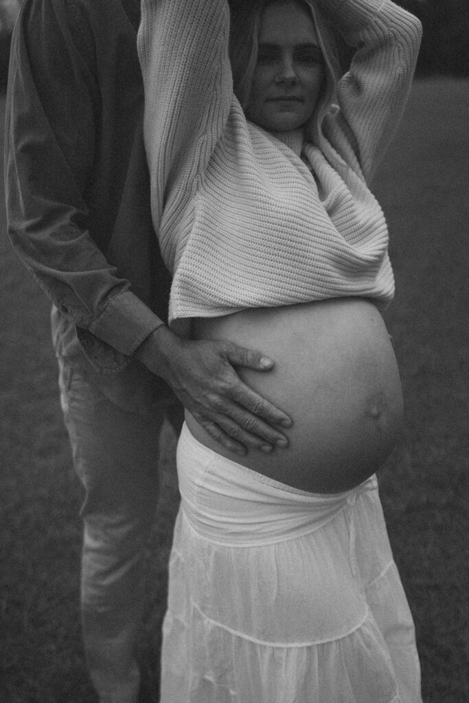 A woman with her hands in the air and her husband holding her belly.