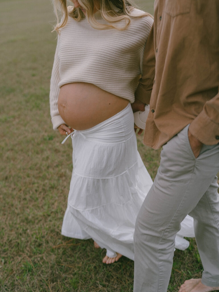 A couple holding hands while the woman holds her pregnant belly.