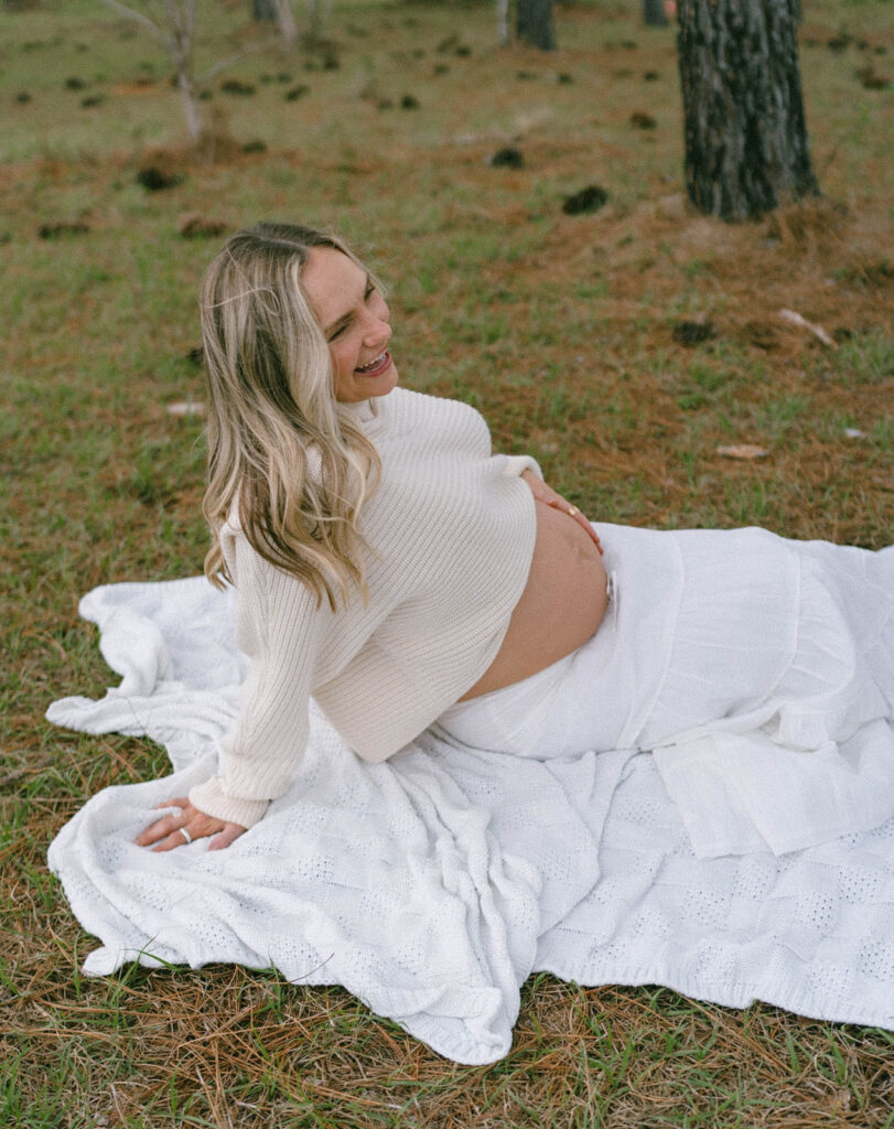 A woman laughing and holding her belly while sitting on a blanket.