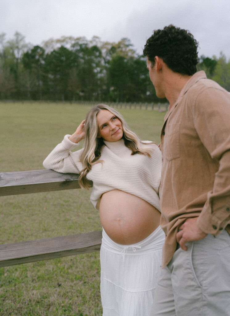 A woman leaning on a fence and looking up at her husband.