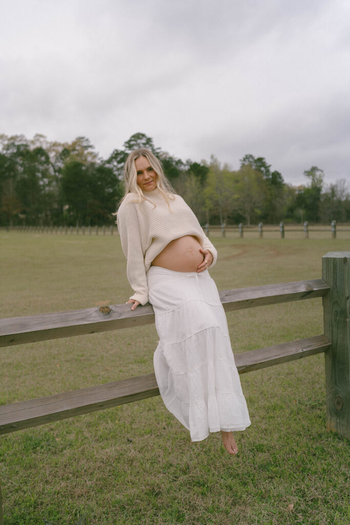 A woman sitting on a fence, holding her belly.