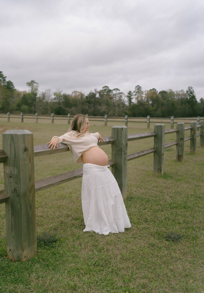 A woman leaning back against a fence, looking off into the distance.
