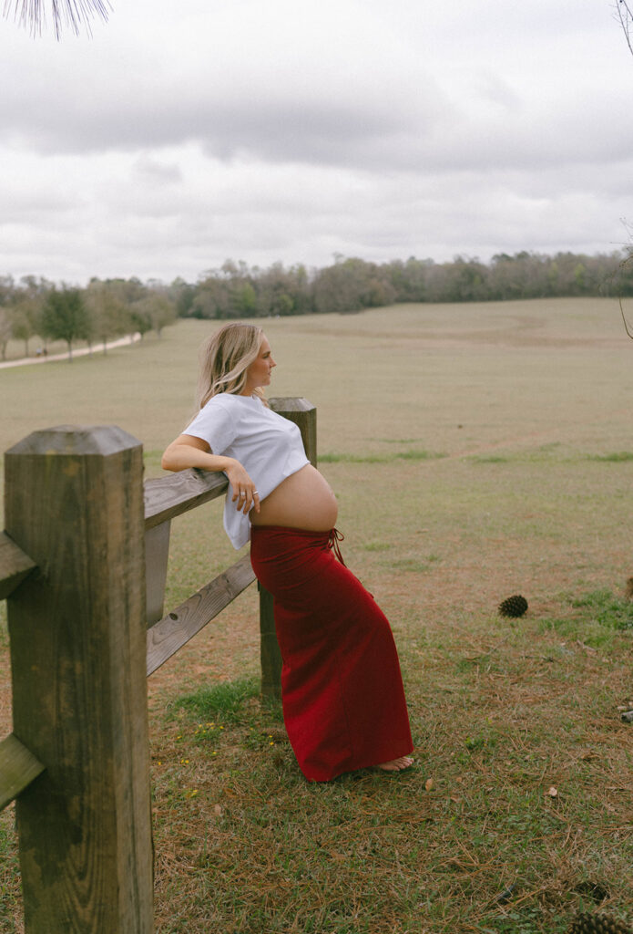 A woman leaning against a fence for maternity photos.