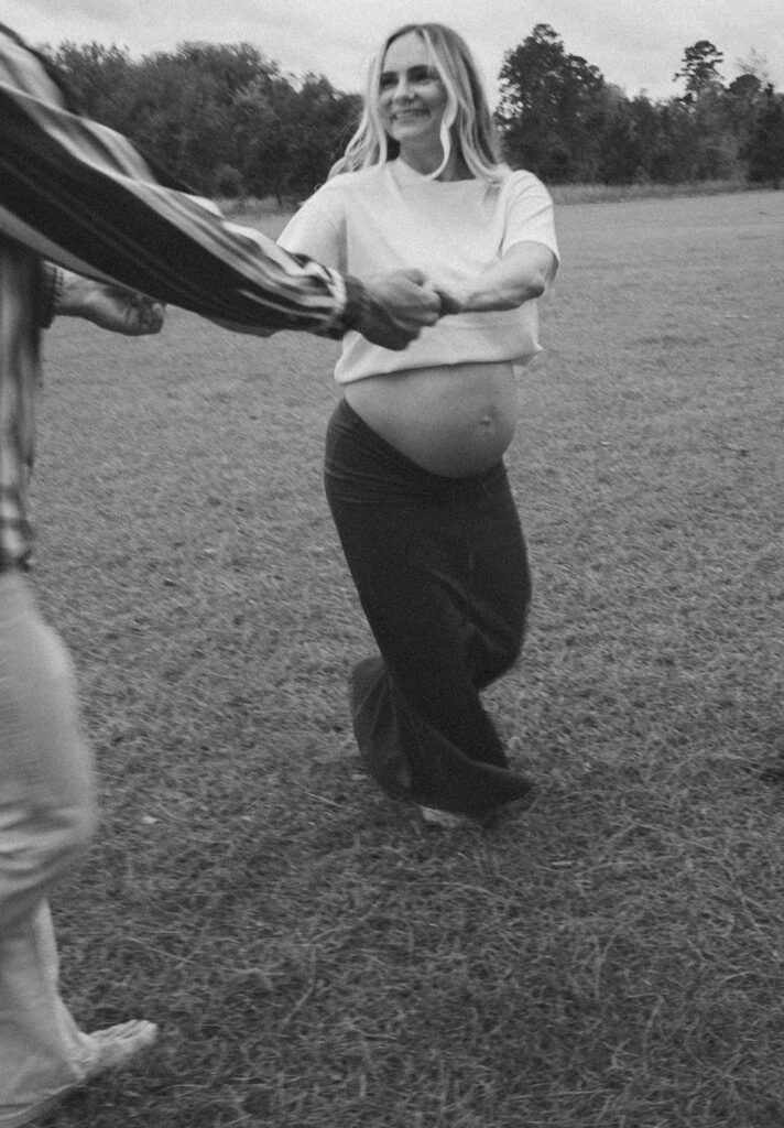 Maternity photos of a man and woman holding hands and spinning around in a field.