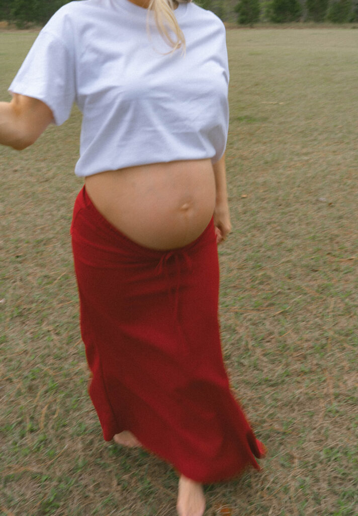 A woman walking in a red skirt for maternity photo outfit ideas.