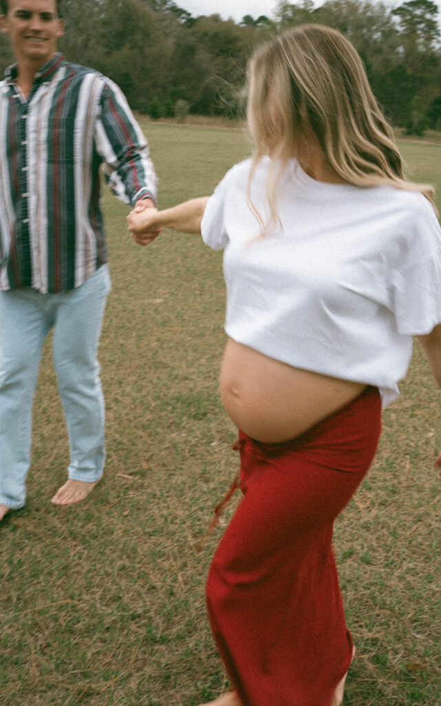 Maternity photos of a couple holding hands and walking at a park in Tallahassee.