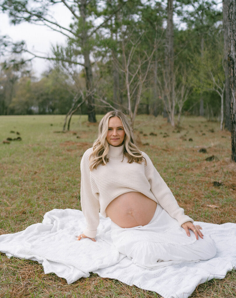 A woman sitting on a white blanket at J.R. Alford Greenway during maternity photos.
