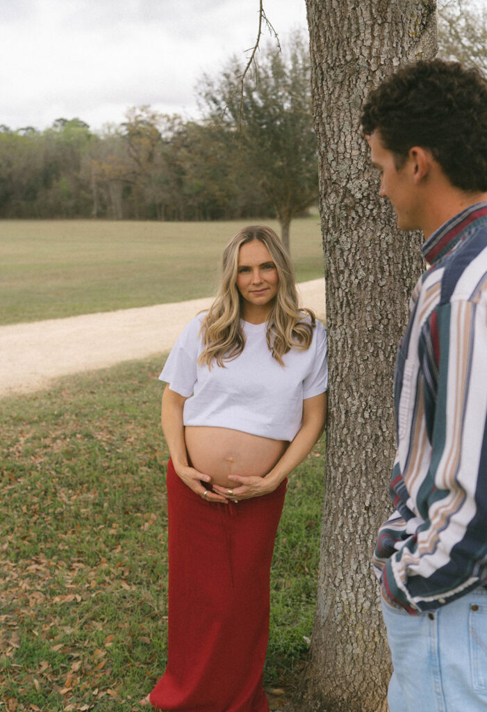 A pregnant woman leaning against a tree while her husband looks at her.