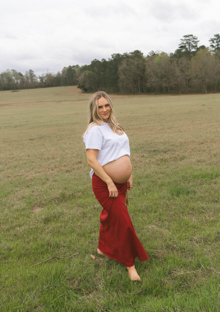 A woman holding her red skirt while she poses for maternity photos.
