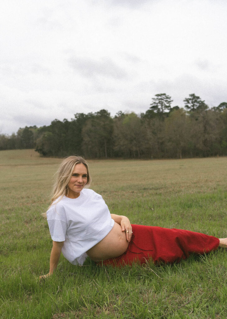Maternity photos of a woman lying in the grass, holding her belly.