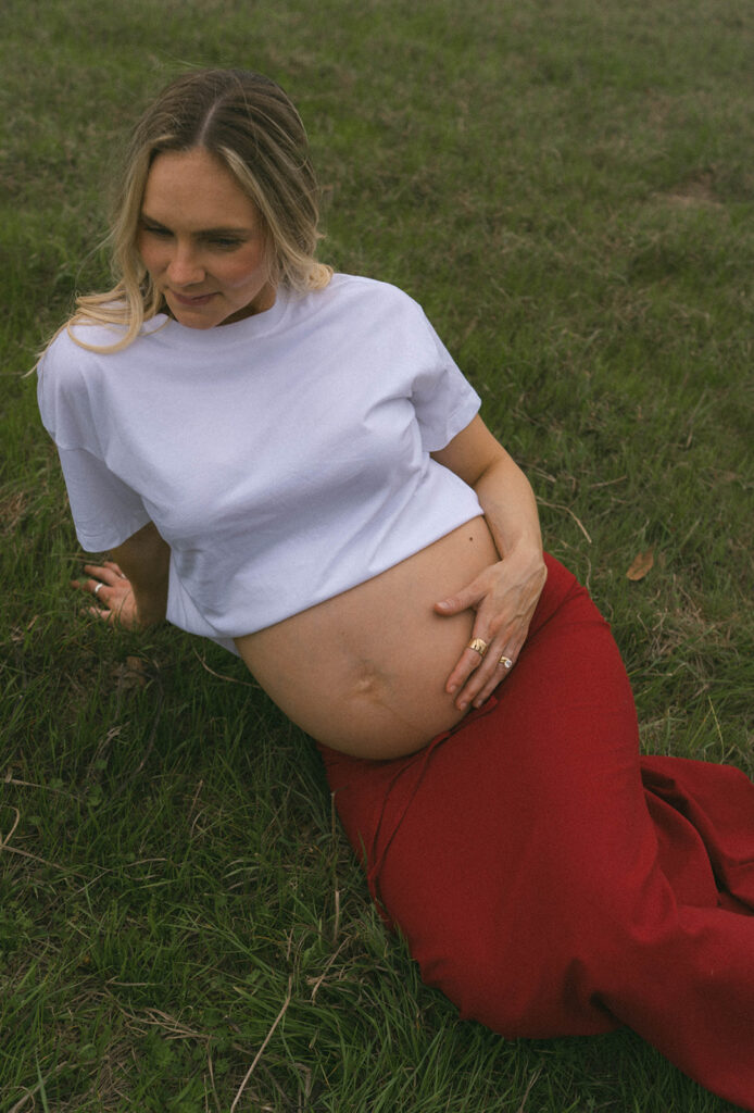 A woman lying in the grass, holding her baby belly.