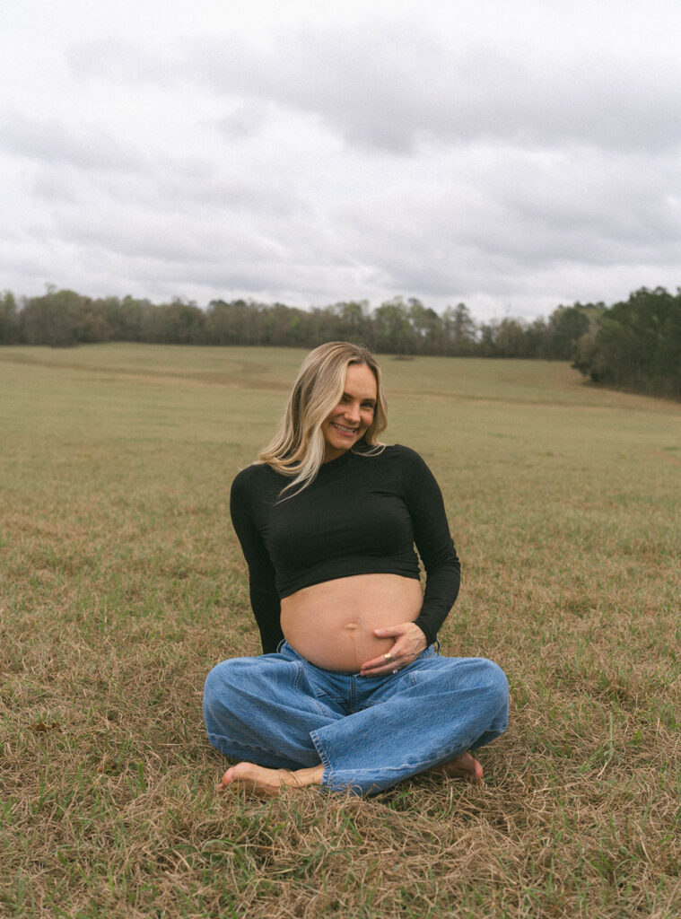 A woman smiling and sitting cross-legged in a field in Tallahassee.
