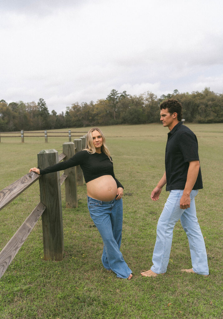 A pregnant woman leaning against a fence while her husband walks towards her.