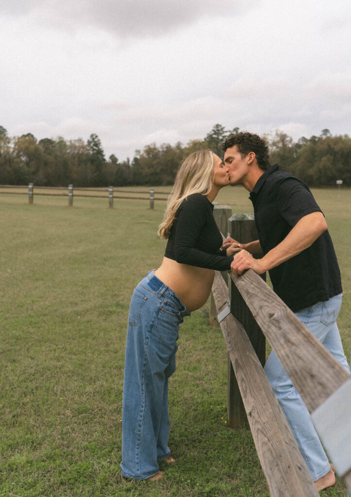 Maternity photos of a couple kissing over a wooden fence at J.R. Alford Greenway in Tallahassee.