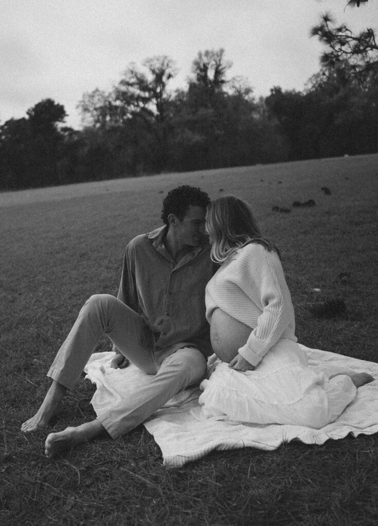 A couple sitting on a blanket about to kiss for romantic maternity photos poses.