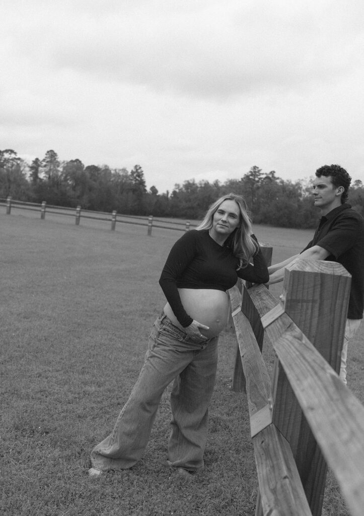 A woman playing with her hair by the fence as her husband looks at her.
