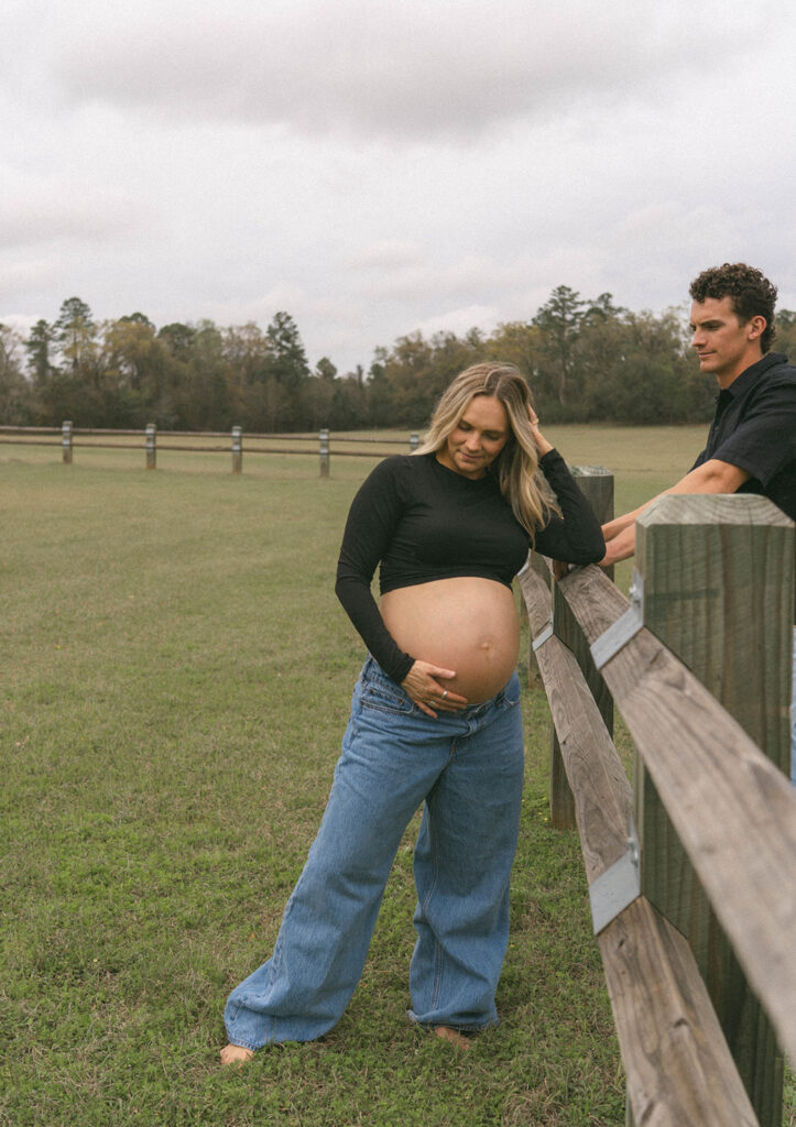 A woman holding her pregnant belly while her husband admires her.