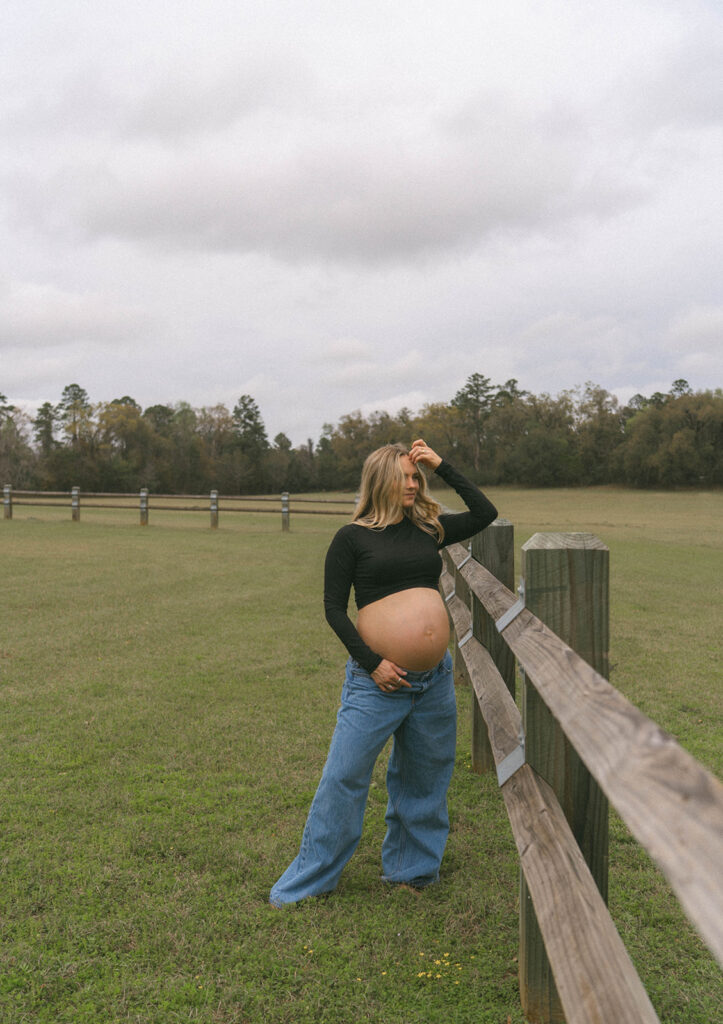 A pregnant woman looking off into the distance while adjusting her hair in the wind.