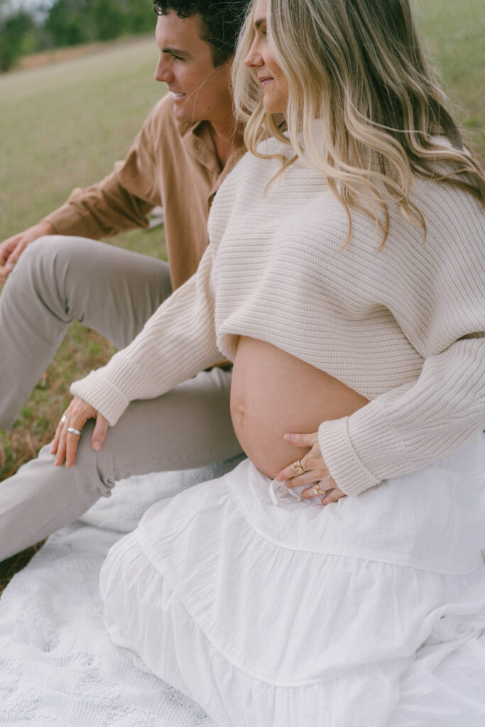 A couple sitting on a white blanket while looking off into the distance for maternity photos.