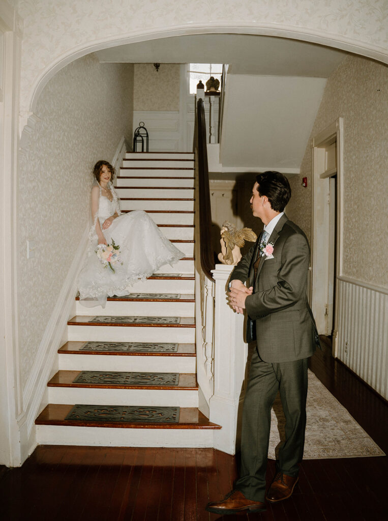 Bride sitting on the staircase while the groom looks at her. 