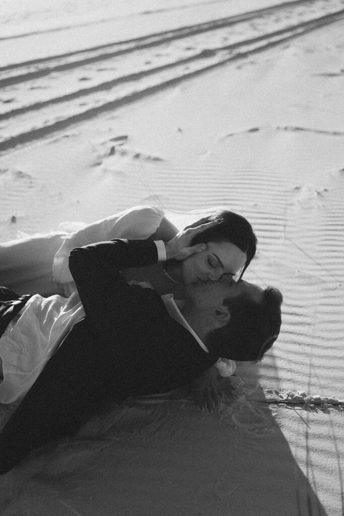 Bride and groom kissing while laying in the sand during their Florida beach elopement.