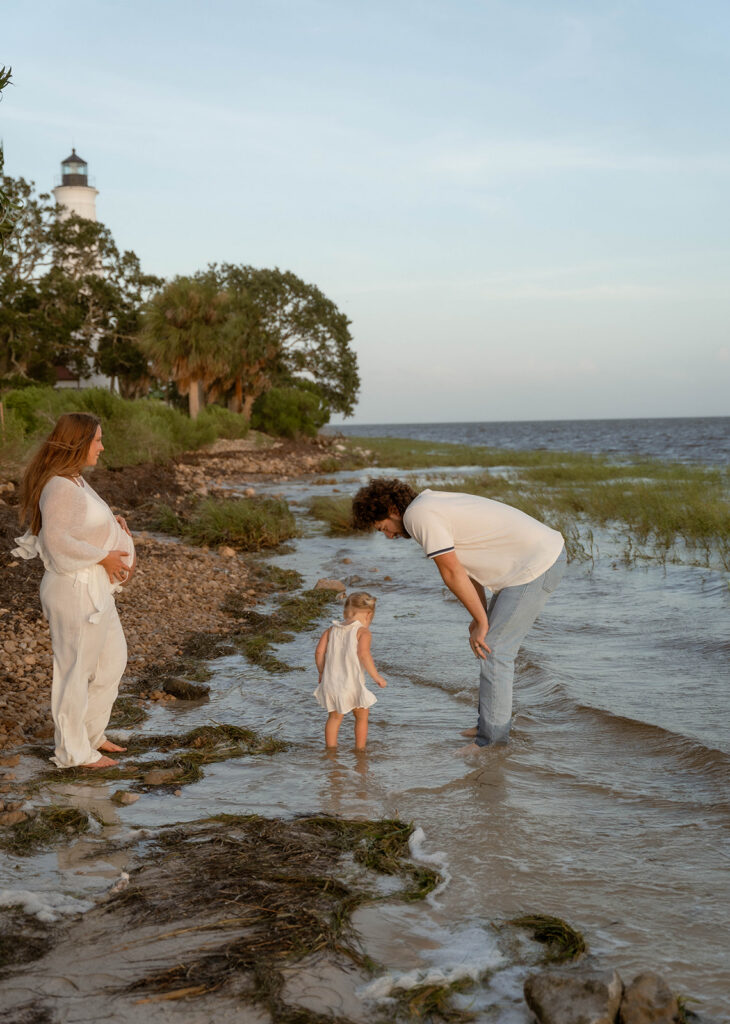 Parents standing in the water with their toddler for family maternity photos.