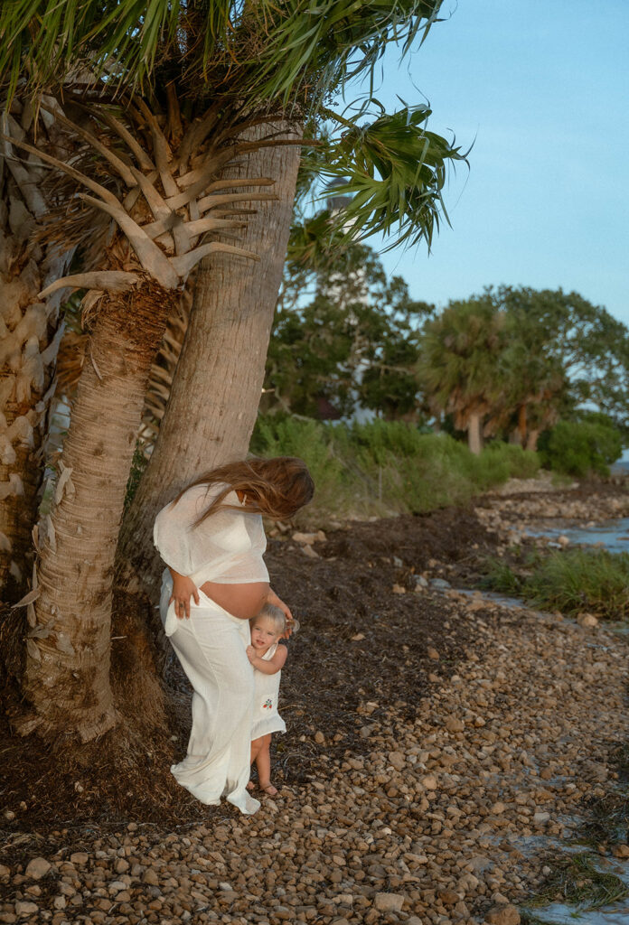 A toddler hugging her mother by a palm tree.