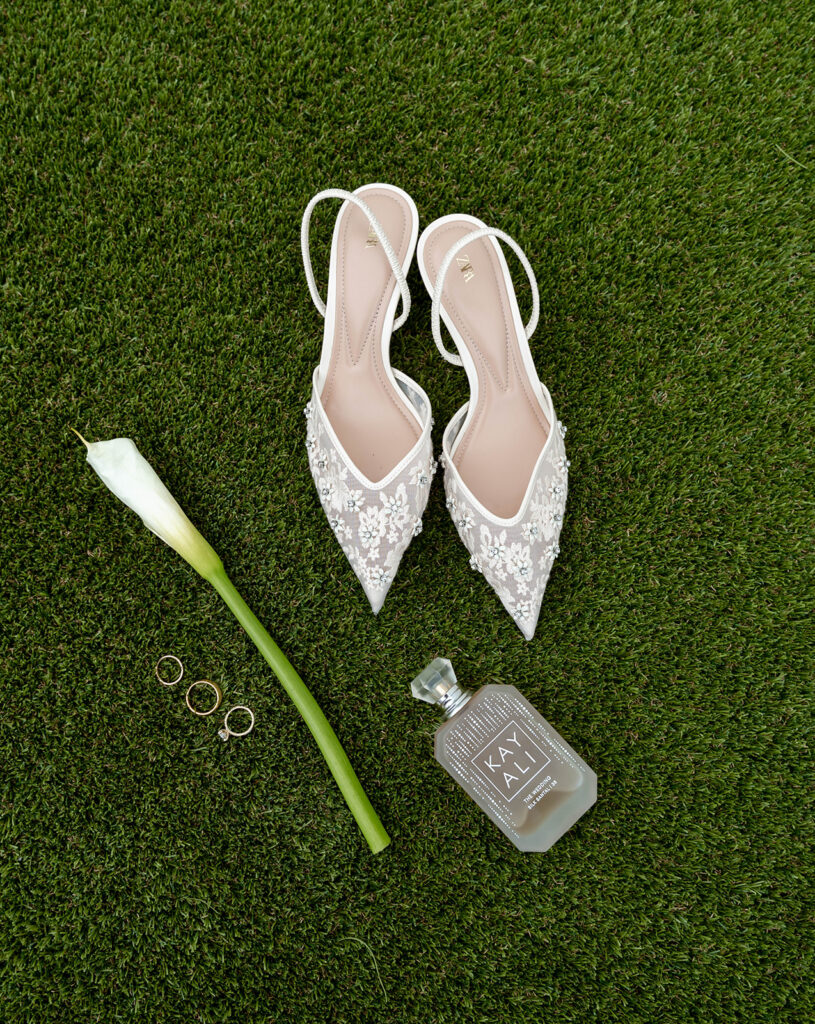 Wedding heels, perfume, wedding rings, and a flower.