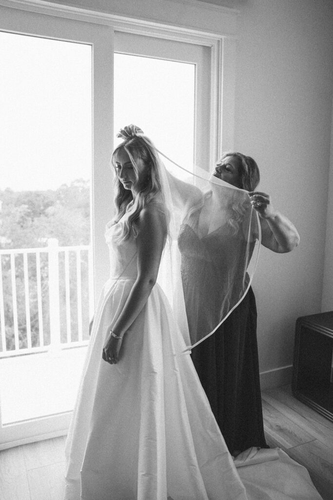 Mother of the bride helping the bride put on her veil. 